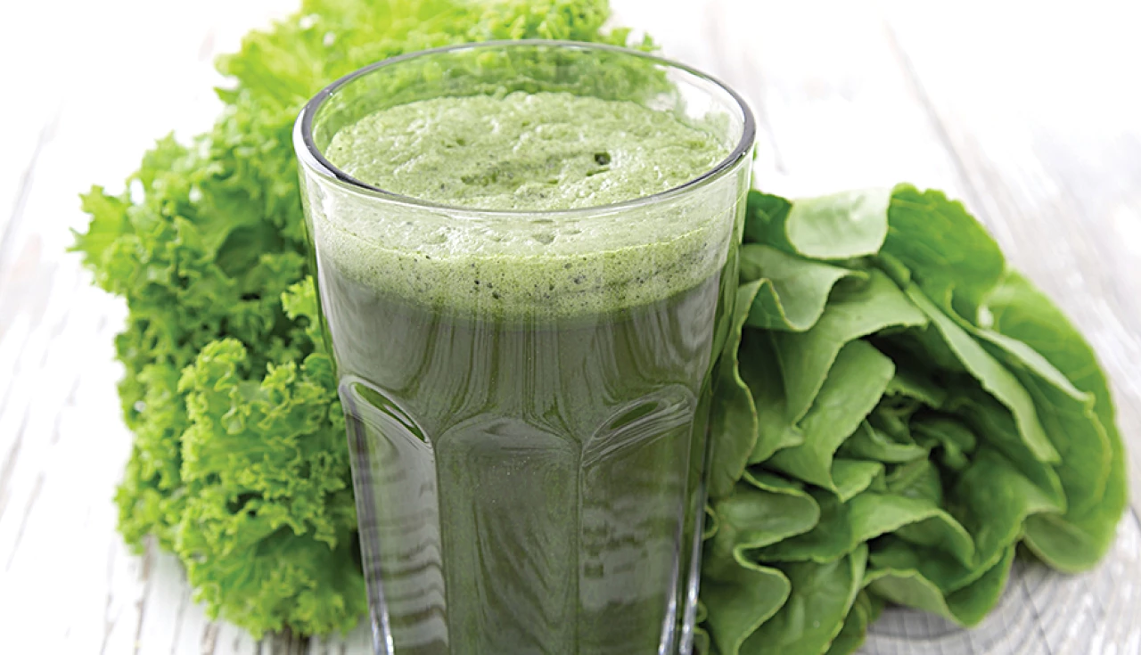 a glass of green smoothie next to lettuce